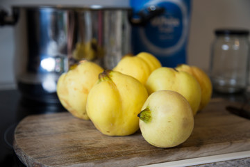 Freshly picked homegrown organic yellow quinces with big stainless steel stock pot, sugar and empty jar, with wooden chopping board on stove top.