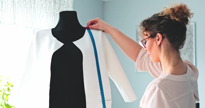 Tailor measuring lady jacket on mannequin at fashion design workshop