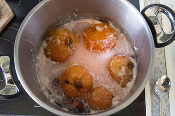 Top view of quinces simmering in a large stainless steel pot in a sugar syrup. They have turned ruby red from the tannins in the fruit and are now ready to be removed to make jelly and then paste.