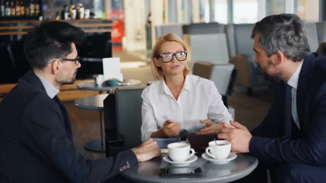 Smiling senior businesswoman is discussing work with male partners handsome men during informal meeting in cafe. Business, people and communication concept.
