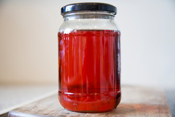 Homemade quince jelly in a glass jar with a black lid sitting on a wooden chopping board. It is made with imperfect, organic homegrown fruit. The clear ruby red color comes from the tannins.