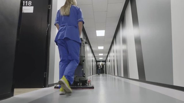 Female worker cleaning floor with machine.