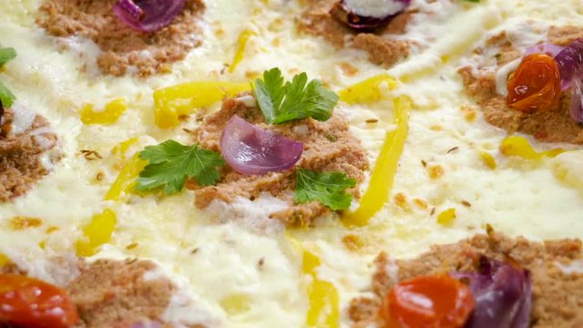 Italian food. Delicious traditional pizza topped with cream sauce, fresh parsley, dried tomatoes, red onion, parmesan cheese, bell pepper, minced beef meat, cumin seeds. Slow motion. HD