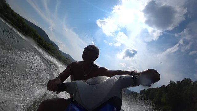 muscular guy rides on the river on a jet ski. riding a jet ski on a mountain river. blue sky with clouds, water splashes and turns on jet ski. front view from the first person. stock video footage.