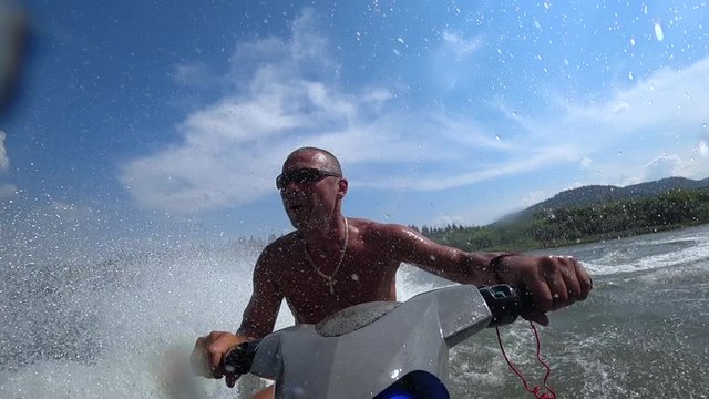 muscular guy on a jet ski. riding a jet ski on a mountain river. beautiful squall of water close-up, splashes of water and turns on jet ski. front view. bright sky. stock videos. super slow motion