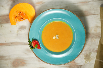 Pumpkin soup puree in a blue plate with pumpkin seeds. Light wooden background.