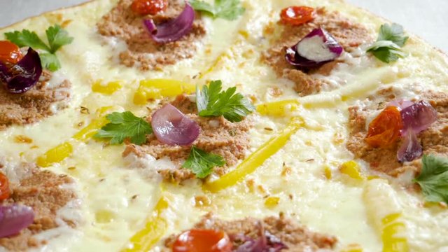 Italian food. Delicious traditional pizza topped with cream sauce, fresh parsley, dried tomatoes, red onion, parmesan cheese, bell pepper, minced beef meat, cumin seeds. Slow motion. HD