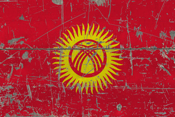 Grunge Kyrgyzstan flag on old scratched wooden surface. National vintage background.