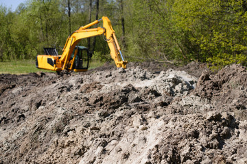 Big heap of soil with working excavator at the background at constructing new asphalt road at countryside near forest
