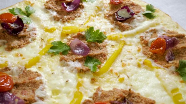 Italian food. Delicious traditional pizza topped with cream sauce, fresh parsley, dried tomatoes, red onion, parmesan cheese, bell pepper, minced beef meat, cumin seeds. Slow motion. HD