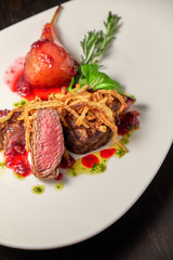 Meat steak with pear on a white plate. Dark wooden background. Restaurant food.
