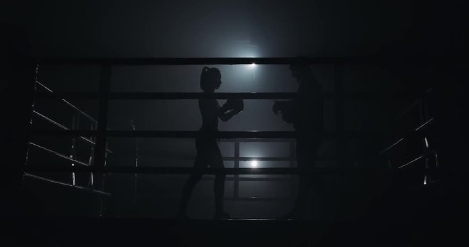 Female boxer and her coach preparing to training on the boxing ring. Silhouette. Boxing concept
