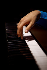 Fototapeta na wymiar one male hand on the piano. The palm lies on the keys and plays the keyboard instrument in the music school. student learns to play. hands pianist. black dark background. vertical
