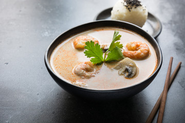 Tom yam kung spicy thai soup with shrimp, seafood, coconut milk, chili pepper and rice in black bowl. Close up.