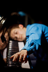 young man sitting at the piano. the boy lies on the keys and plays the keyboard instrument in the music school. student learns to play. hands pianist. black dark background. vertical