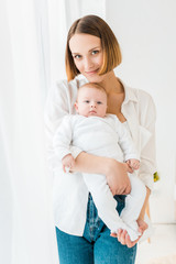 Smiling young mother in white shirt holding baby at home