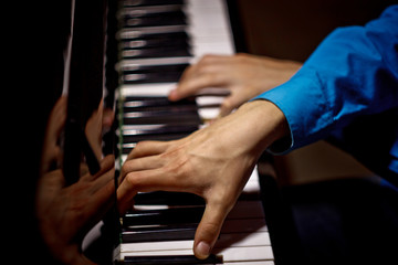 Obraz na płótnie Canvas two male hands on the piano. palms lie on the keys crosswise and play the keyboard instrument in the music school. student learns to play. hands pianist. black dark background. top view