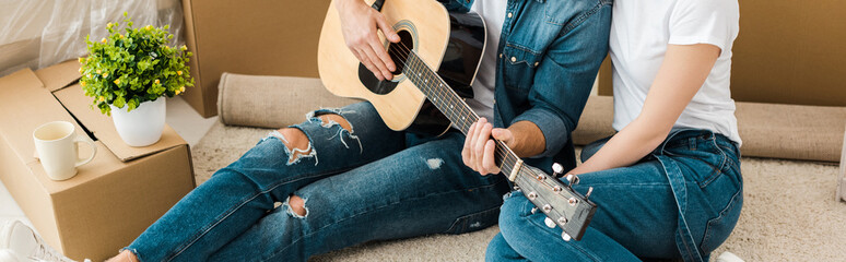 Panoramic shot of man sitting on carpet with wife and playing acoustic guitar