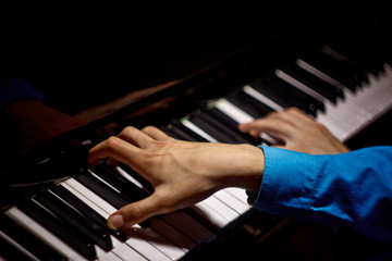 Fototapeta na wymiar two male hands on the piano. palms lie on the keys crosswise and play the keyboard instrument in the music school. student learns to play. hands pianist. black dark background. top view