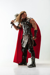 Long hair and muscular male model in leather viking's costume with the big hammer cosplaying Thor isolated on white studio background. Full-lenght portrait. Fantasy warrior, antique battle concept.