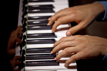Fototapeta na wymiar two male hands on the piano. palms lie on the keys and play the keyboard instrument in the music school. student learns to play. hands pianist. black dark background. top view