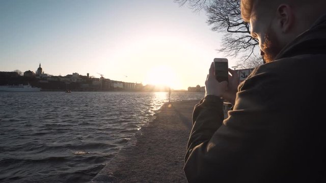 Bearded smartphone tourist taking cell phone photos in Stockholm Sweden. Sunset golden hour in Scandinavia. Close up gimbal footage.