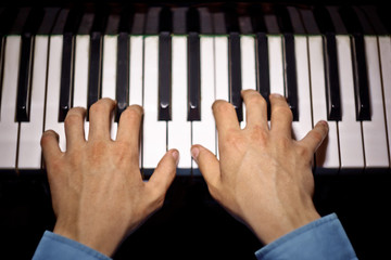 two male hands on the piano. palms lie on the keys and play the keyboard instrument in the music school. student learns to play. hands pianist. black dark background. top view