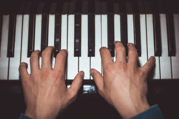 two male hands on the piano. palms lie on the keys and play the keyboard instrument in the music school. student learns to play. hands pianist. black dark background. top view