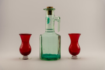 old corked bottle and red shot glasses on a white back ground