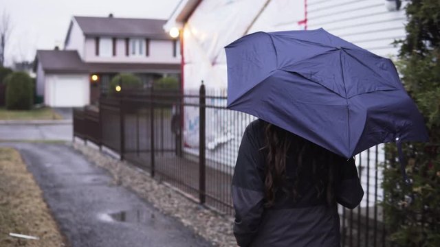 Teenage girl walking down sidewalk and opening umbrella.