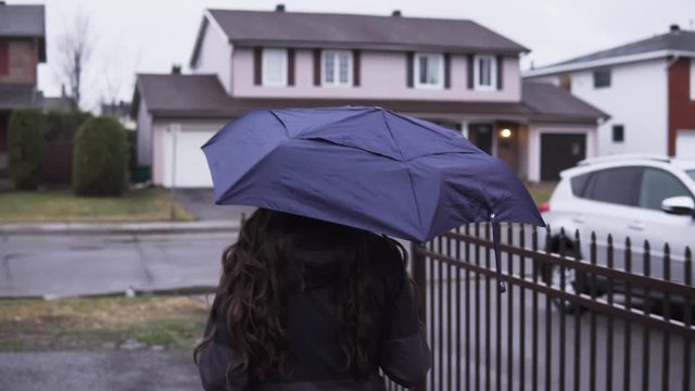 Girl walking down in a neighborhood with an umbrella.