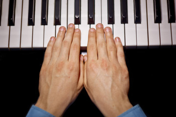 two male hands on the piano. palms lie on the keys and play the keyboard instrument in the music school. student learns to play. hands pianist. black dark background. top view