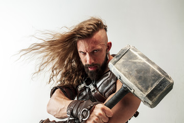 God of thunder. Blonde long hair and muscular male model in leather viking's costume with the big hammer cosplaying Thor isolated on white studio background. Fantasy warrior, antique battle concept. - obrazy, fototapety, plakaty