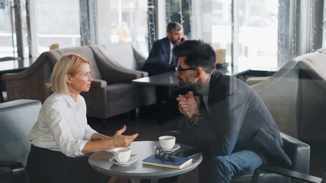 Business partners senior woman and mature man are discussing cooperation in cafe talking during lunch break. Human communication and negotiations concept.