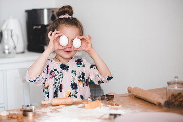 Fototapeta na wymiar Smiling kid girl 4-5 year old having fun with raw eggs in kitchen. Making cookies indoors. Childhood.