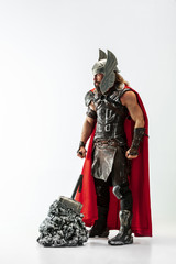 Fototapeta premium Long hair and muscular male model in leather viking's costume with the big hammer cosplaying Thor isolated on white studio background. Full-lenght portrait. Fantasy warrior, antique battle concept.