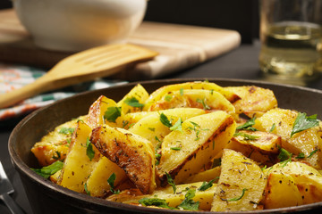 Baked potatoes with spices and parsley in a pan on a black background