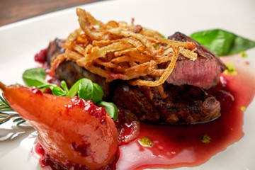 Meat steak with pear on a white plate. Dark wooden background. Restaurant food.