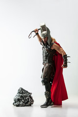 Fototapeta premium Long hair and muscular male model in leather viking's costume with the big hammer cosplaying Thor isolated on white studio background. Full-lenght portrait. Fantasy warrior, antique battle concept.