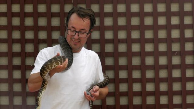 Caucasian male holds a python around his neck for the first time. Man looks nervous. COPY SPACE.