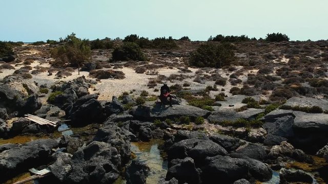 Drone panning shot of model sitting at an amazing paradise island beach Elafonissi, Crete