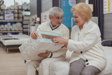 Charming senior woman laughing joyfully, shopping for new orthopedic mattress with her loving...