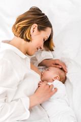 Mother in white shirt lying on bed and breastfeeding baby