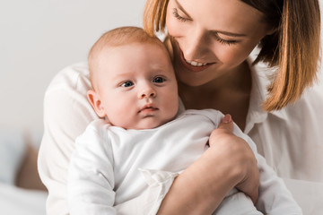 Smiling young mother in white shirt holding baby at home