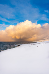 Snow and sea: the snow arrives all the way to the shoreline of an unfrozen deep blue sea while the...