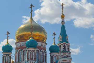 Fototapeta na wymiar Domes of religious buildings. Crosses on the domes of the church. The cathedral with golden and green domes against the blue sky with clouds in the rays of the sun.