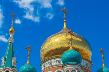 Domes of religious buildings. Crosses on the domes of the church. The cathedral with golden and green domes against the blue sky with clouds in the rays of the sun.