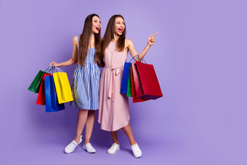 Full length body size photo two people beautiful she her models chic ladies carry many packs direct empty space laugh laughter fellowship wear casual dresses isolated purple violet bright background