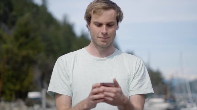 Slow Motion Man Standing On Wooden Pier In Marina Using Smartphone In The Summer