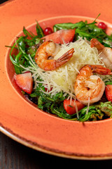 Fresh salad of arugula, shrimp and strawberry. Dark wooden background. Restaurant menu